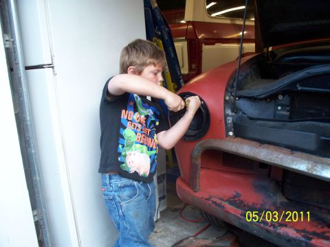 1990 Ford Bronco - A young boy is seen working on the headlight of a red vehicle, with another vehicle partially visible in the background.