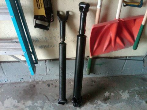 1979 Ford Bronco - Two driveshafts are shown in a garage setting with various tools and equipment.