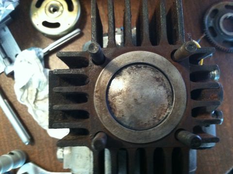 1981 Garelli Rally Sport - A close-up view of a motorcycle engine cylinder and piston, surrounded by various mechanical parts on a wooden surface.