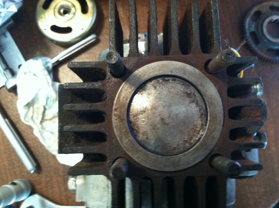Close-up of a rusty motorcycle engine cylinder with a piston visible. Other engine parts are scattered around
