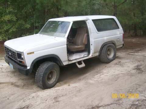1983 Ford Bronco - This 1980s Ford Bronco is parked in a sandy area with trees. The doors are open, revealing the interior.