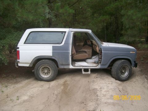 1983 Ford Bronco - Side view of a Ford Bronco with its door open, sitting on a sandy surface.