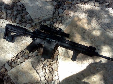 1996 Ford Bronco - An assault rifle with a scope and tactical grip rests on a bed of rocks.