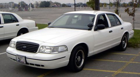 1999 Ford Crown Victoria - A white sedan is parked in a lot next to another white sedan.