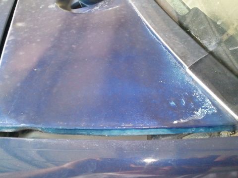1994 Ford Bronco - Close-up of a blue car's hood edge, showing wear and a gap between panels.