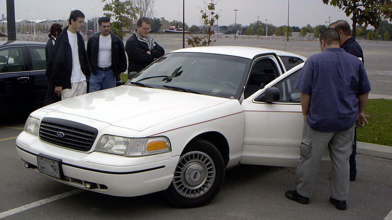 White 1999 Ford Crown Victoria, front passenger door open, with people gathered around