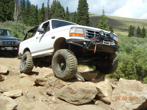 1996 Ford Bronco - A white Ford Bronco tackles a challenging rocky trail with another vehicle visible in the background.