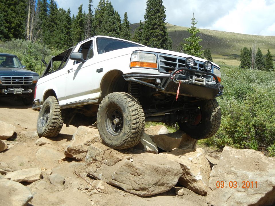 White Ford Bronco with off-road modifications navigating rocky terrain