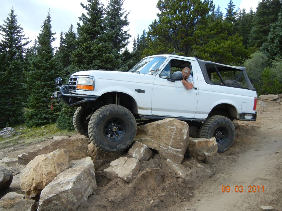 White 1996 Ford Bronco on rocks, driver visible