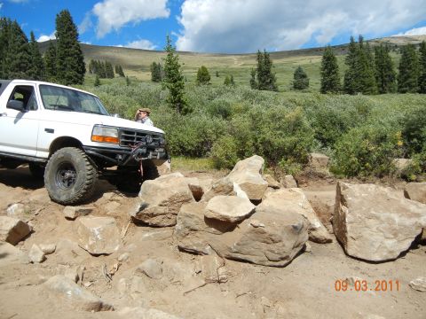 1996 Ford Bronco - 1996 Ford Bronco tackling a challenging rocky trail under a partly cloudy sky.