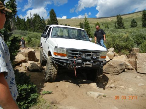 1996 Ford Bronco - A white 1996 Ford Bronco is shown tackling a challenging off-road course on a sunny day.
