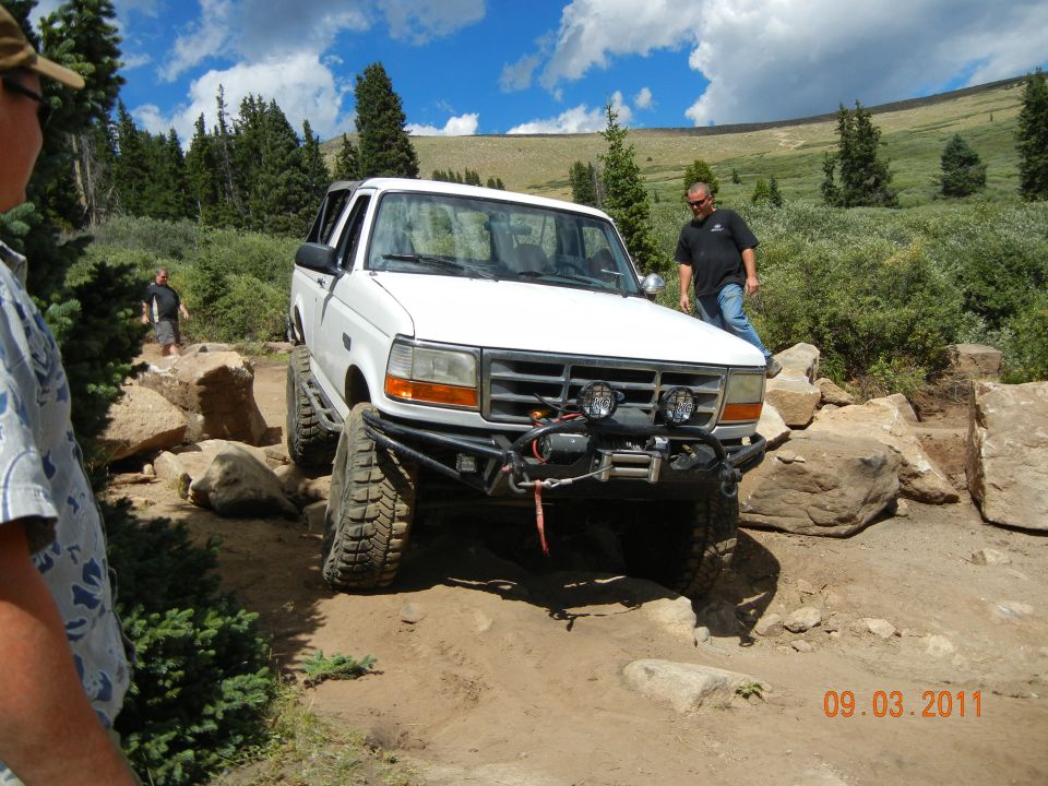 White 1996 Ford Bronco navigating a rocky trail with a man standing nearby