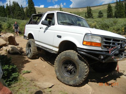 1996 Ford Bronco - A white 1996 Ford Bronco navigates a rocky off-road trail under a partly cloudy sky.