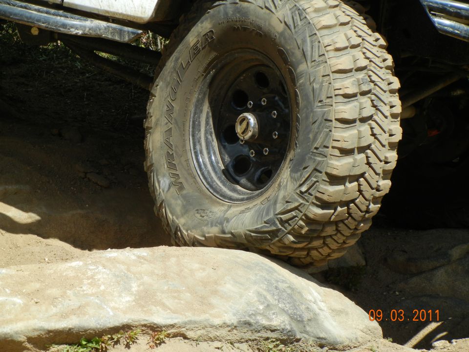 Close-up of a knobby off-road tire on a black rim, angled over a rock