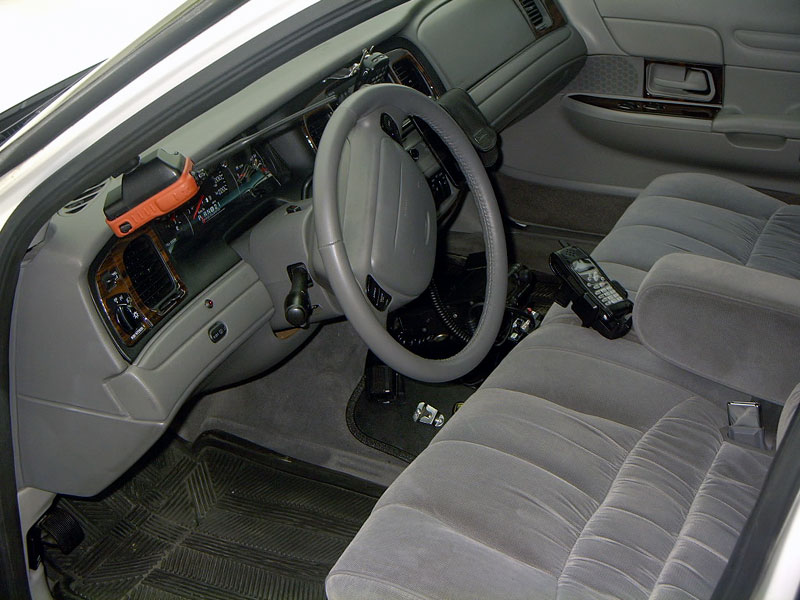 Gray fabric interior of a 1998 Ford Crown Victoria, showing dashboard, steering wheel, and front seats with a car phone