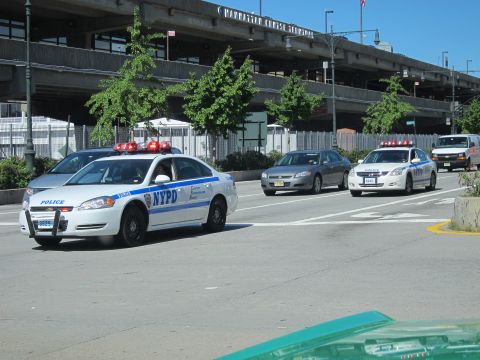 1991 Ford LTD Crown Victoria - Two white NYPD patrol cars with roof lightbars drive on a city street beneath an elevated highway structure.