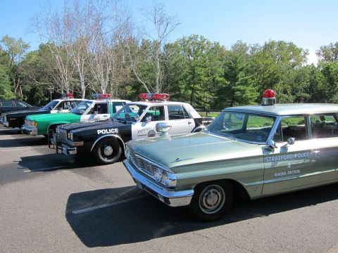 1991 Ford LTD Crown Victoria - light green Stratford Police Radio Patrol station wagon with a red roof beacon leads a row of classic police cars.