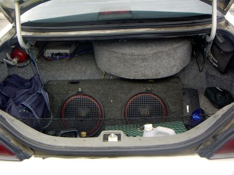 1999 Ford Crown Victoria - The trunk of a car is filled with audio equipment, including subwoofers and an amplifier, along with a spare tire and other items.