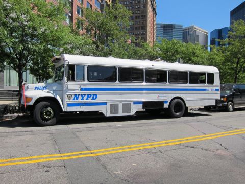 1991 Ford LTD Crown Victoria - blue and white NYPD Police bus is parked along a city street with high-rise buildings and trees in the background.