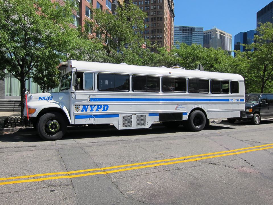 Blue and white NYPD police bus parked on a city street lined with tall buildings