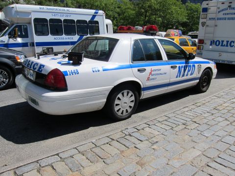 1991 Ford LTD Crown Victoria - white NYPD Ford Crown Victoria patrol car numbered 1448 sits on cobblestones beside police vans and an Access-A-Ride bus.