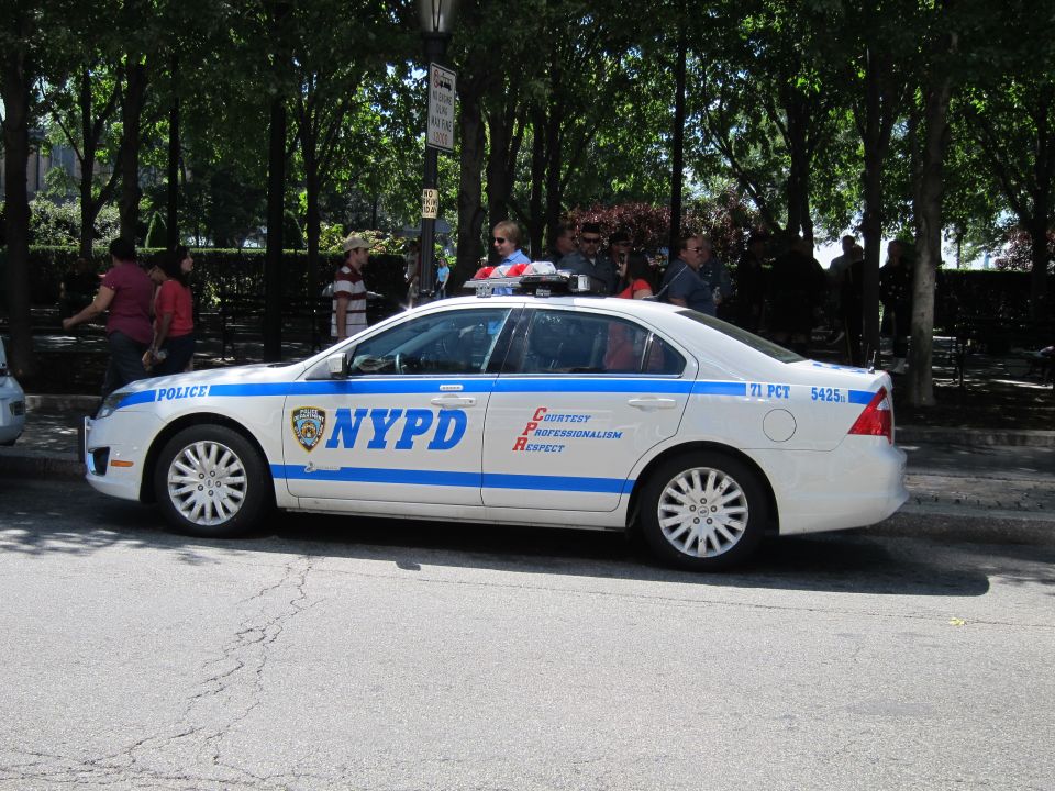 White and blue NYPD sedan parked along a park fence in the city