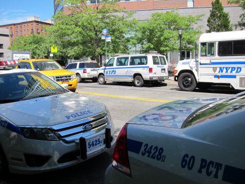1991 Ford LTD Crown Victoria - Multiple police vehicles including a Ford patrol car, NYPD van and bus crowd a sunny city street.