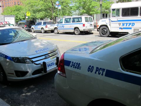 1991 Ford LTD Crown Victoria - NYPD patrol cars marked 60 PCT alongside a department van and bus on a tree-lined city street.