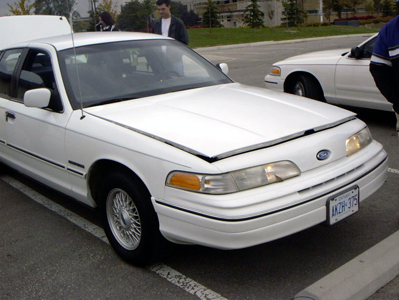 White 1999 Ford Crown Victoria front view, hood open. Another white Crown Victoria visible