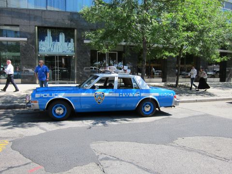 1991 Ford LTD Crown Victoria - vintage blue NYPD Highway 3 patrol sedan with blue wheels parked along the curb in front of a glass building.