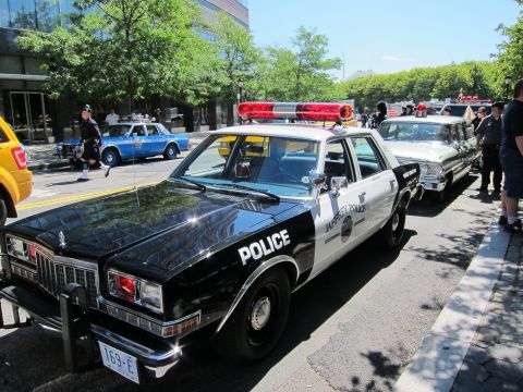 1991 Ford LTD Crown Victoria - row of black-and-white vintage police sedans, including a Chevrolet, lined up at a curbside vehicle display.