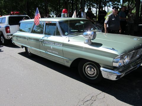 1991 Ford LTD Crown Victoria - vintage green Stratford Police radio-patrol station wagon with a spotlight and US flag parked at an outdoor event.