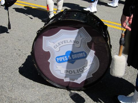 1991 Ford LTD Crown Victoria - maroon bass drum with a Cleveland Police Pipes & Drums shield emblem, carried by a marcher with a mallet in a parade.