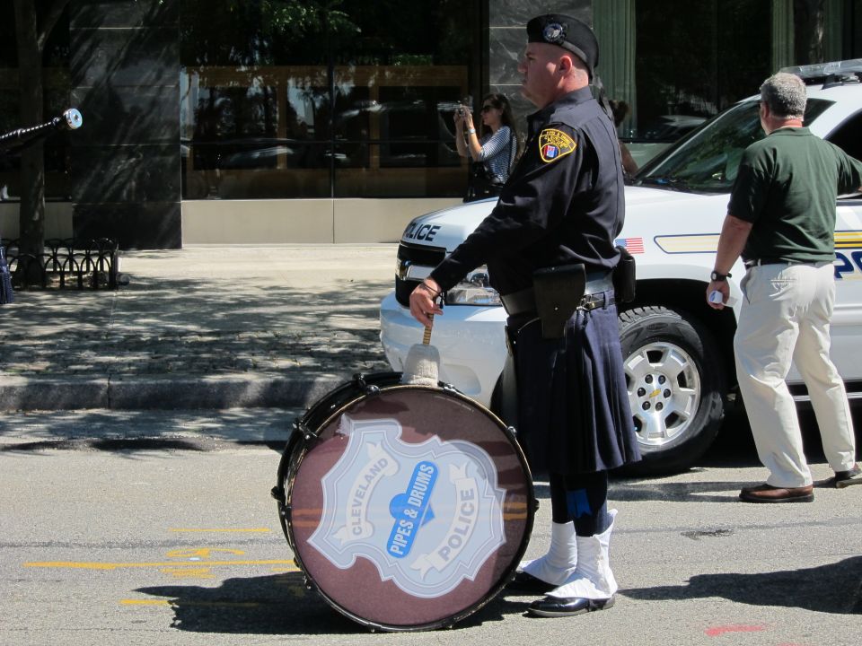 Drummer holding a bass drum reading Cleveland Police Pipes & Drums beside a police SUV