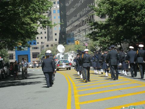 1991 Ford LTD Crown Victoria - procession of officers in dress uniforms with white caps marches along a wide city avenue past parked vehicles and a satellite truck.
