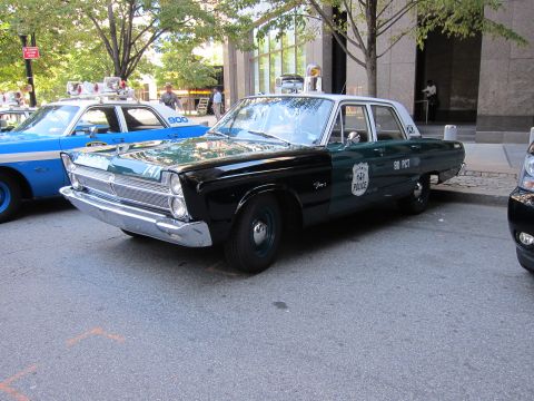 1991 Ford LTD Crown Victoria - green-and-black vintage Plymouth police sedan marked 80 PCT sits parked on a tree-lined city street near other cars.