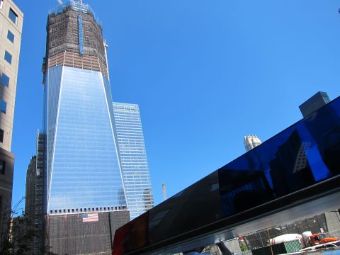 1991 Ford LTD Crown Victoria - tall glass skyscraper under construction flies an American flag, viewed over the dark reflective roof of a vehicle.