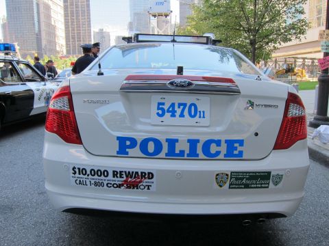 1991 Ford LTD Crown Victoria - Rear view of a white Ford Police hybrid sedan marked POLICE with plate 547011 and a $10,000 reward Call 1-800-COP-SHOT decal.
