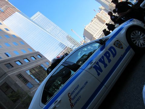 1991 Ford LTD Crown Victoria - low-angle shot shows a white-and-blue NYPD patrol sedan tilted against a backdrop of glass office skyscrapers.