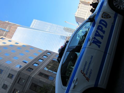 1991 Ford LTD Crown Victoria - white-and-blue NYPD patrol sedan lettered Courtesy Professionalism Respect sits below tall glass skyscrapers under a clear sky.