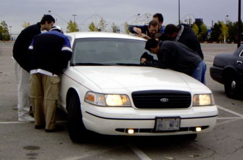 1999 Ford Crown Victoria - A group of people examine the front of a white 1999 Ford Crown Victoria sedan.