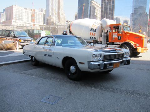 1991 Ford LTD Crown Victoria - 1970s white New York State Police four-door sedan sits in a lot with a concrete mixer and orange truck behind it.
