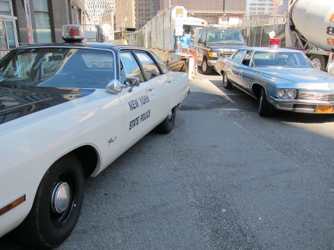 1991 Ford LTD Crown Victoria - white New York State Police sedan is parked beside a light-blue station wagon near a cement mixer and SUV.
