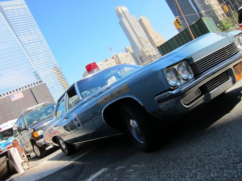 1991 Ford LTD Crown Victoria - light-blue early-1970s Police sedan with a roof beacon sits at a low angle against a backdrop of skyscrapers.