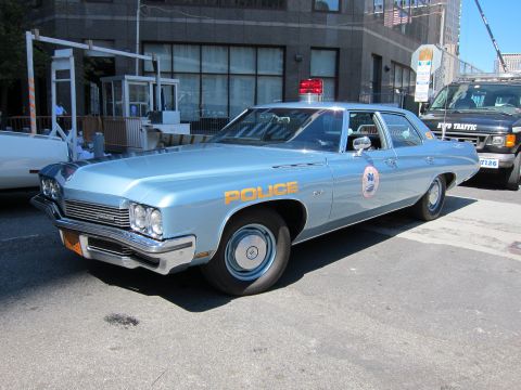 1991 Ford LTD Crown Victoria - light-blue 1970s Police sedan with a circular department seal is parked beside a dark NYPD Traffic van.