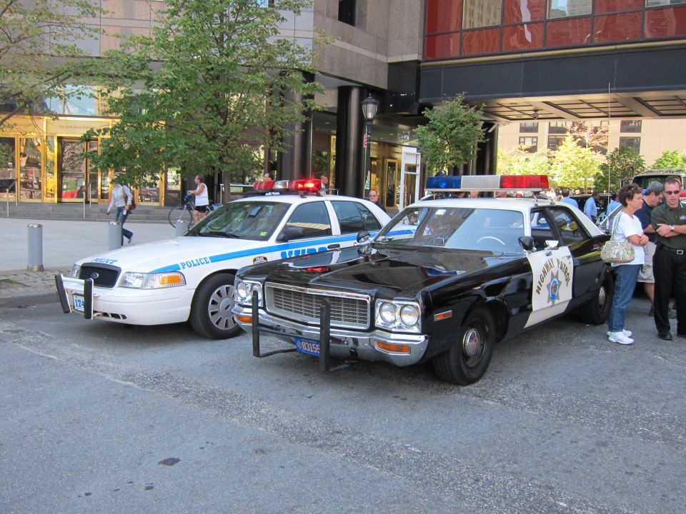 White modern police sedan beside a black-and-white vintage Highway Patrol cruiser