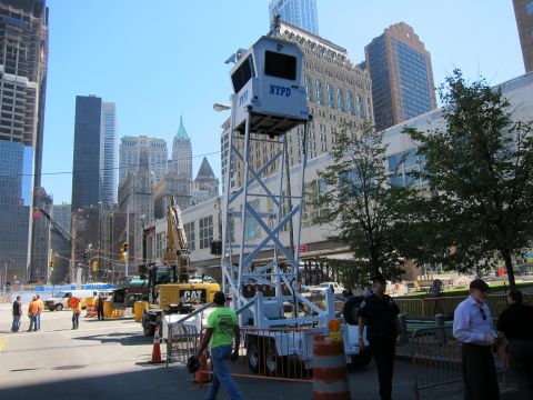 1991 Ford LTD Crown Victoria - NYPD elevated observation booth on a steel frame stands at a busy street corner with construction equipment and pedestrians.