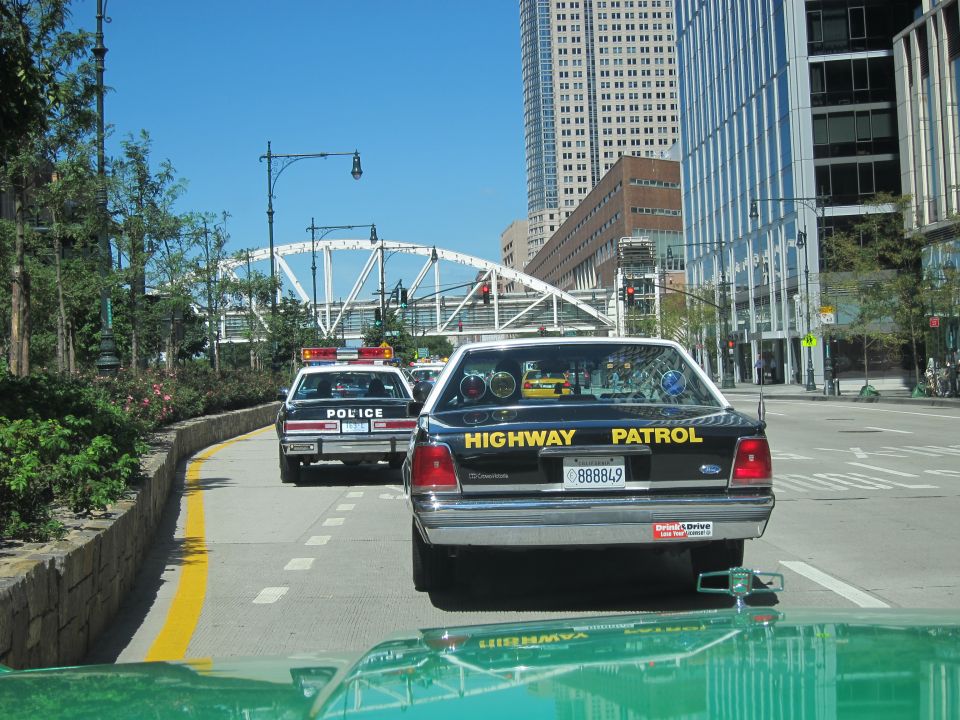 Black Highway Patrol Crown Victoria following a white police car on a city street