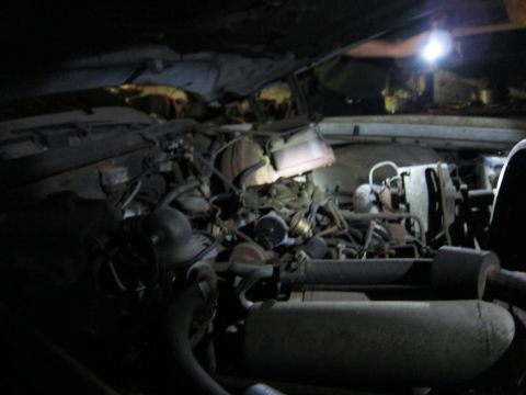 1991 Ford LTD Crown Victoria - The engine bay of a vehicle, showing various components like the carburetor and hoses under dim lighting.