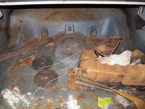 1991 Ford LTD Crown Victoria - The interior of a car trunk shows significant rust and debris, including wood and paper items.
